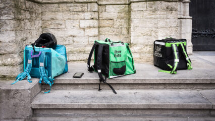 Des sacs de livreurs à vélo sont alignés sur le parvis d'une église.