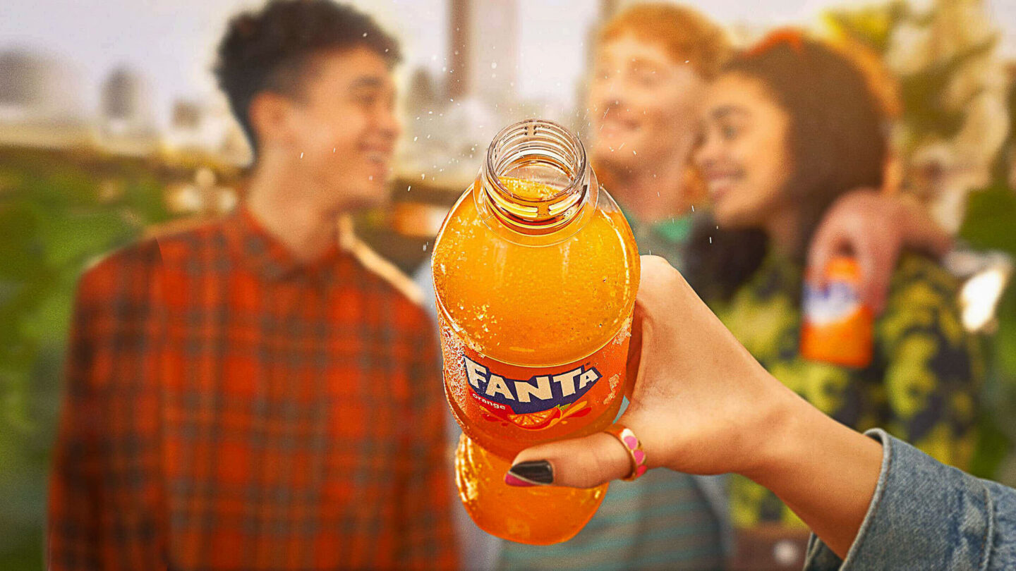 Un main tient une bouteille de Fanta, une boisson couleur orange.