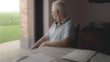Eddy, éleveur atteint de la maladie de Parkinson, assis à la table de sa maison, devant ses piles de documents.