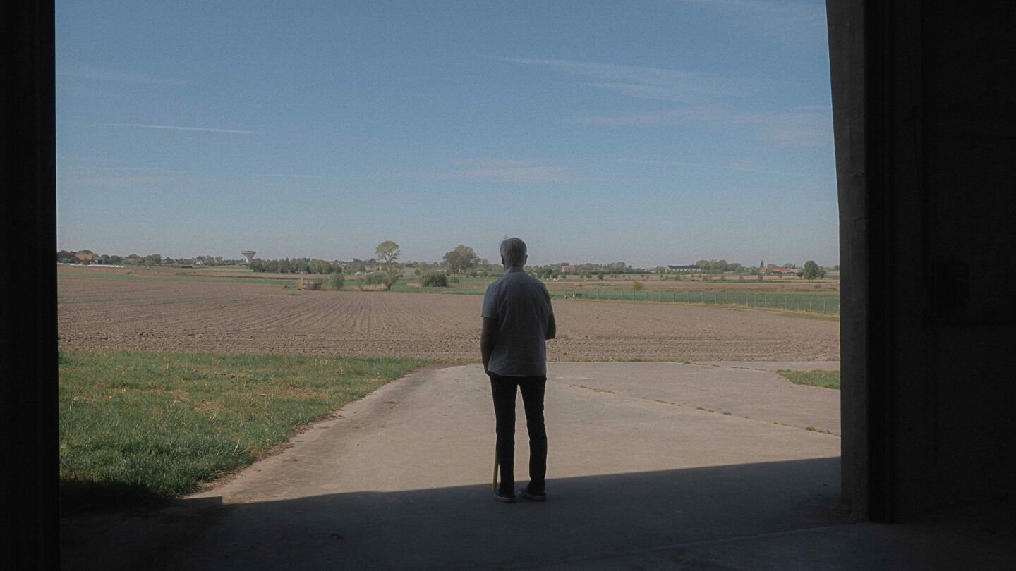 Marc, agriculteur de 52 ans se tient debout, face à un de ses champs, à la sortie de son hangar.