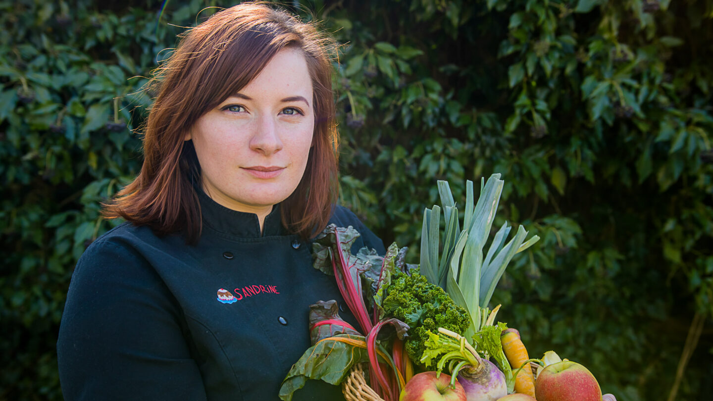 Photo en plan américain, sur fond de buissons, de Sandrine Dagneau, patronne du restaurant Rosalie (Gembloux).