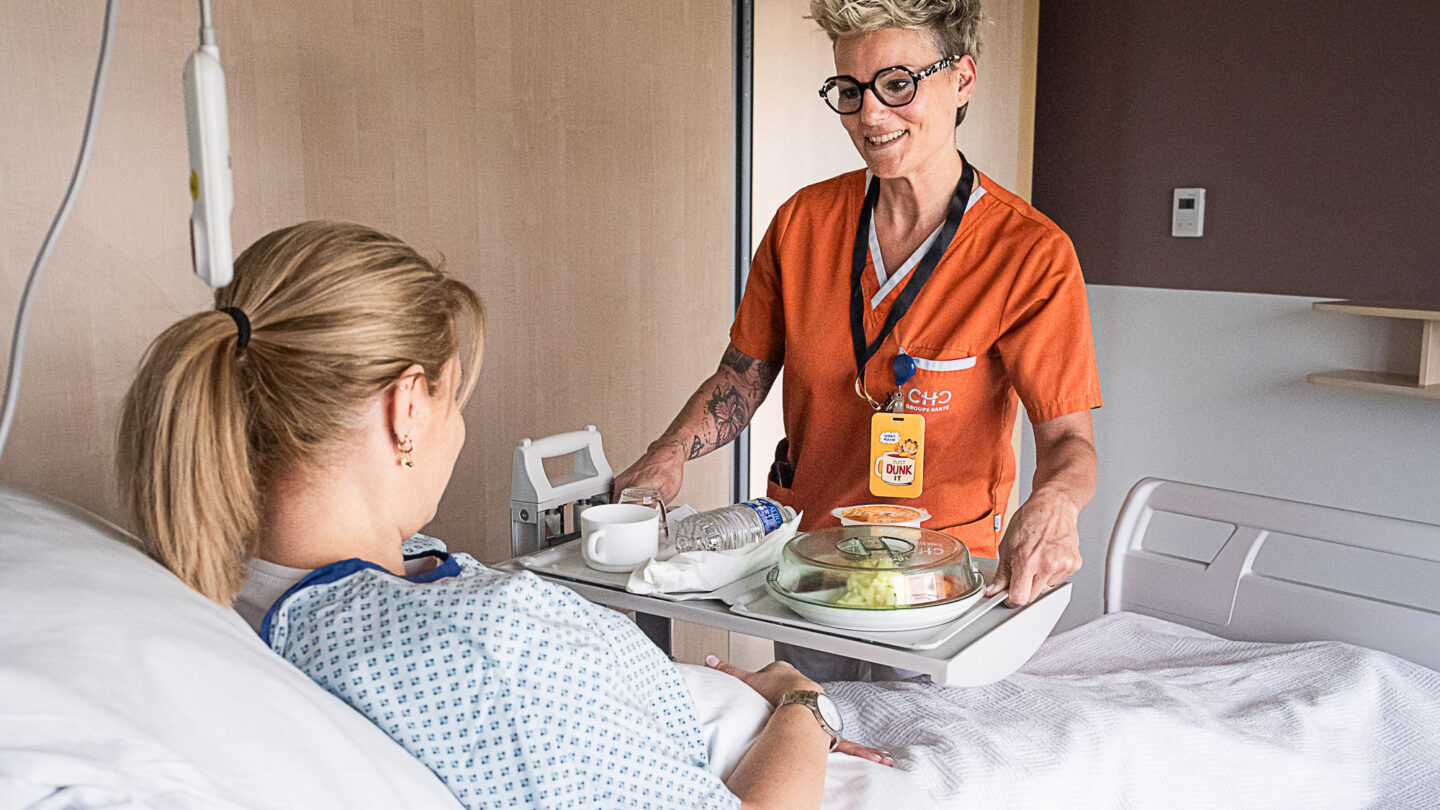 Une aide hôtelière sert un plateau-repas à une patiente au CHC Montlegia.