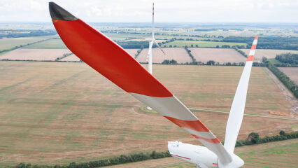 Vue de pales d'éolienne donnant sur un champ agricole.